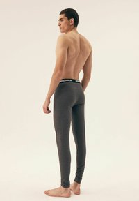 Gray leggings with a fitted design and a black waistband featuring the brand name. The model is shown from the back, barefoot.
