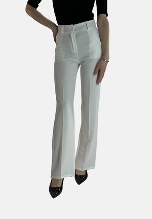 Witte high-waisted flared broek met voorplooien, een gladde textuur en een getailleerde pasvorm, gecombineerd met zwarte puntige hakken.