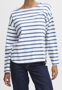 Langärmliges Shirt mit weißen und blauen horizontalen Streifen. Weicher Stoff mit lockerem Schnitt und weitem Rundhalsausschnitt. Seitliche Schlitze am Saum.