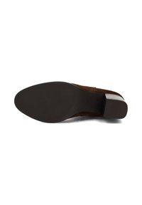 Zapato de ante marrón con punta cerrada, tacón grueso y suela de goma texturizada, que presenta una sección suave en el lateral para facilitar el calzado.