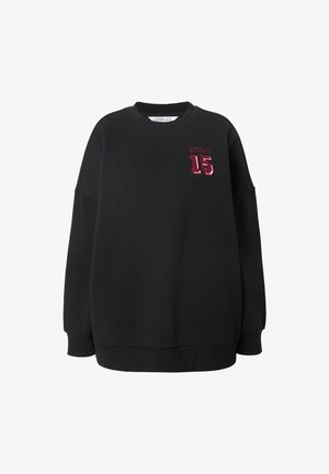 Sweatshirt noir avec un col rond, coupe ample, épaules tombantes, et un "STUDIO 15" brodé bordeaux sur le devant. Matière en coton doux.