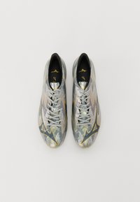 Sportschoenen met een metallic zilveren afwerking, een gestructureerd oppervlak, zwarte binnenvoering en gele accenten in het ontwerp en de branding.
