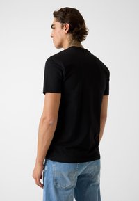 Zwarte korte mouw t-shirt gemaakt van glad katoen, met een klassieke ronde hals en een standaard pasvorm, gezien van achteren.