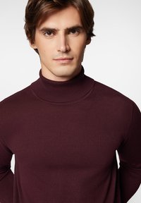 Bordowy sweter z golfem, wykonany z materiału o prążkowanej fakturze. Posiada wysoki kołnierz i długie rękawy, dopasowany krój oraz miękką teksturę.