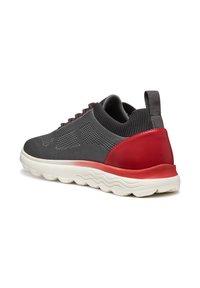 Sneaker grigio in maglia con accenti rossi sul tallone, tomaia testurizzata, design con lacci e suola spessa bianca con un motivo ondulato.