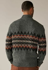 Pull en tricot gris avec un col montant, arborant une bande à motifs en orange, noir et blanc. Fini texturé et poignets côtelés.