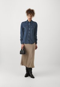 Denimskjorte med knappestilling, to brystlommer; beige satin midi skjørt; svarte knelang støvletter; liten svart håndveske.