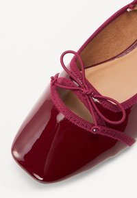 Ballerines en cuir verni bordeaux avec un bout carré, détail en nœud en satin et un bord élastique autour de l'ouverture pour un ajustement sécurisé.