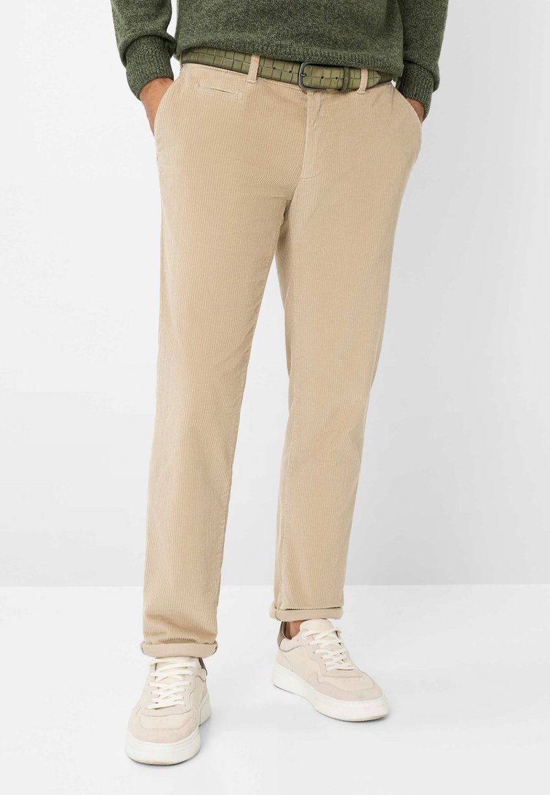 Pantaloni in corduroy beige con design a gamba dritta e tasche frontali, abbinati a sneakers bianche e una cintura verde testurizzata.