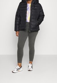 Černá vycpaná bunda s kapucí, nošená přes pastelové tričko s technikou tie-dye. Úzké šedé džíny a bílé sportovní boty. Důraz na pohodlí a teplo.