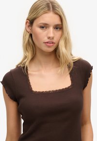 Top marrón acanalado con un escote cuadrado y un borde de encaje con volantes. Las mangas cortas y con volantes añaden textura al diseño ajustado.