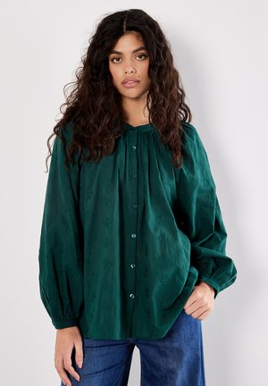 Mörkgrön blus med knäppning, plisserad halsringning, lång ärm och texturerat blommönster. Matchas med blå denim.