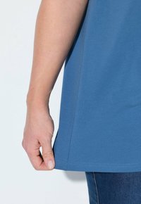 T-shirt in cotone blu con orlo curvo, caratterizzato da maniche corte e spacchi laterali. Cuciture dettagliate lungo l'orlo, texture liscia.
