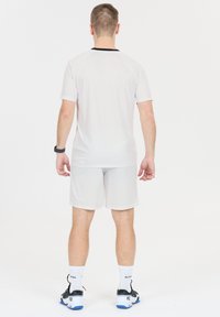 Vaaleanharmaa urheilupaita, jossa on raglan-hihat ja musta kaulus, yhdistettynä vastaaviin shortseihin. Varustettu mustilla ja sinisillä urheilukengillä.