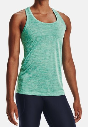 Débardeur de sport vert sans manches porté par une personne à la peau foncée, associé à un legging bleu marine, sur un fond blanc uni.