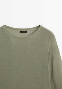 Pull en maille vert olive clair avec un col rond et des détails de couture visibles sur l'épaule et le col.