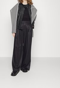 Černá kožená bunda s pruhovanými rukávy, spárovaná s volnými černými kalhotami. Oblečení má texturovaný vzhled a obsahuje jemné kovové detaily.