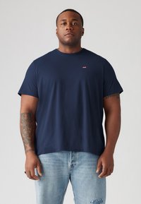 T-shirt en coton bleu marine avec un col rond et des manches courtes, arborant un petit logo rouge Levi's sur la poitrine, associé à un jean léger bleu délavé.