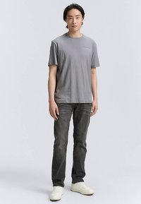 Graues Baumwoll-T-Shirt mit Rundhalsausschnitt und kurzen Ärmeln, kombiniert mit dunkler Jeans und weißen Turnschuhen. Einfaches Design, ohne Muster oder Verzierungen.