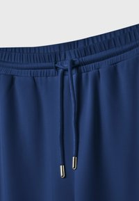 Marineblaue Sporthosen mit einem elastischen Bund, ausgestattet mit einem Kordelzug mit metallischen Spitzen und einer glatten, leichten Stofftextur.