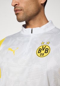 Bílý pulovr na zip se strukturovaným vzorem, žlutými akcenty a logem BVB 09 se dvěma hvězdami. Vyrobeno z syntetického materiálu.
