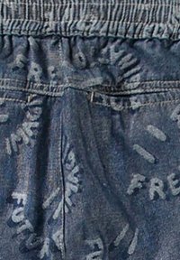 Denim joggers med midja som är elastisk. Har en bleknad blå färg och texturerat tyg, prydd med tryckta detaljer av "FREEDOM" och "FUTURE".