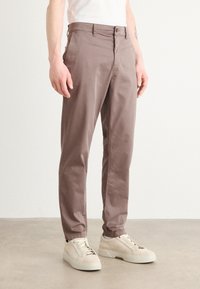 Bruine katoenen broeken met een rechte snit, knoopsluiting, zijzakken en een subtiele stoftextuur, gecombineerd met lichtgekleurde sneakers.