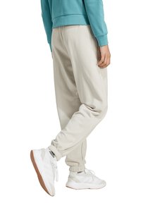 Beige sweatpants with elastic cuffs and a loose fit, paired with white and gray sneakers featuring subtle branding.