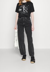 Black graphic t-shirt with white and gray print, high-waisted gray jeans, and black sneakers. Complements include a white bag with studs.