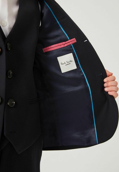 Marinblå kostyjacka med en slät satinfoder, blå piping, en rosa ficka och en vit etikett med texten "Paul Smith Junior."