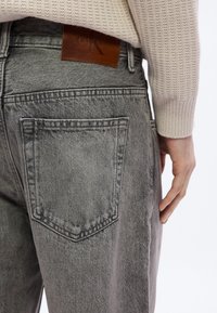 Γκρι τζιν με ξεθωριασμένη υφή, με δύο πίσω τσέπες και καφέ δερμάτινο έμβλημα Calvin Klein πάνω από τη μέση.