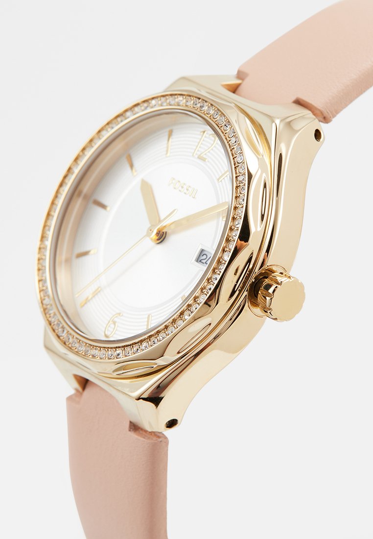 Montre-bracelet dorée avec un cadran blanc, accents en cristal autour de la lunette, et un bracelet en cuir rose clair. Affichage de la date à la position 6 heures.