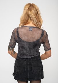 Black sheer top with short sleeves, textured fabric, and subtle gradient pattern. Back features a tag and rounded neckline. Paired with a dark skirt.