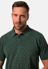Tmavě zelené polo tričko s texturovanou tkaninou, které má jemný černý diamantový vzor a klasický límec se třemi knoflíky.