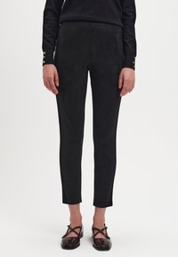 Czarne zamszowe spodnie o slim fit, charakteryzujące się gładką teksturą i skróconą długością, w połączeniu z ciemnobrązowymi butami na paski.