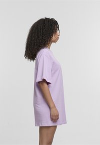 Jasnofioletowy, oversize'owy t-shirt z bawełny z krótkim rękawem, okrągłym dekoltem i luźnym krojem, prezentowany z profilu na jednolitym tle.