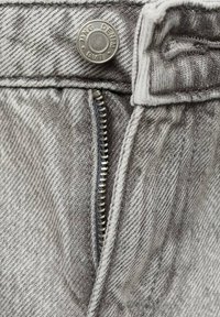 Grå denimjeans i närbild med en silverknapp, blixtlåsdetalj och strukturerad tyg med ett subtilt mönster.