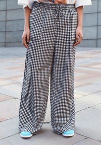 Pantalons large en vichy noir et blanc avec taille élastique et cordon de serrage, dotés de poches latérales et d'une coupe décontractée. Portés avec des baskets bleues.