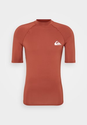 Un rash guard de couleur rouille, fabriqué en tissu lisse. Manches courtes, col haut et logo blanc sur la poitrine gauche. Design ajusté avec des coutures plates.