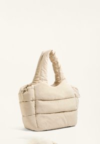 Geantă tote puffy bej, cu două mânere moi, având secțiuni matlasate pentru textură; realizată dintr-un material ușor, cu o formă simplă, rotunjită.