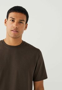 Brązowy t-shirt z krótkim rękawem i okrągłym dekoltem, wykonany z gładkiego materiału, z luźnym krojem i minimalnymi szwami dla wygody.