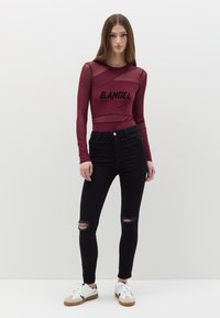 Top de malla burdeos de manga larga con el texto "B.ANGEL", combinado con jeans skinny negros desgastados y zapatillas blancas con suelas beige.