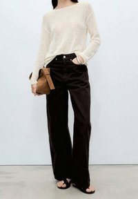 Haut crème en maille à manches longues, associé à un pantalon noir taille haute à jambes larges. Les accessoires comprennent un sac à bandoulière marron et des sandales noires.