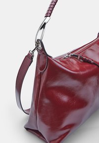 Rode leren handtas met een ronde vorm, gestructureerde afwerking en zilverkleurige hardware. Voorzien van een gevlochten schouderriem en ritssluiting.