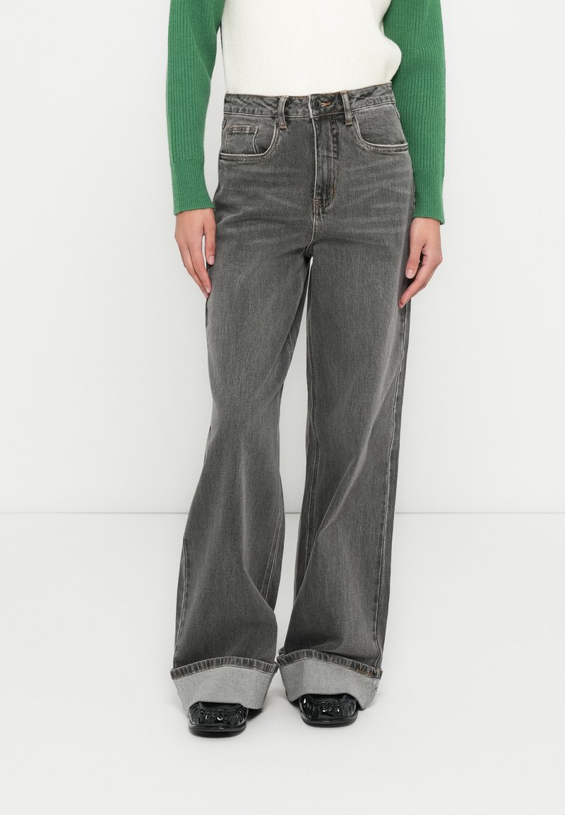 Siv�á džínsy s vysokým pásom a širokými nohavicami s bledým efektom. Majú predné vrecká, viditeľné švy a ohrnuté lemovanie. Skombinované so zeleno-bielym topom.