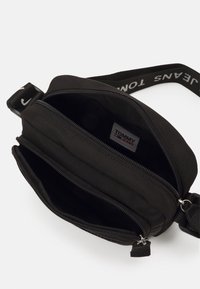 Černá crossbody taška Tommy Jeans se dvěma otevřenými zipovými přihrádkami a nastavitelným popruhem s textem loga.