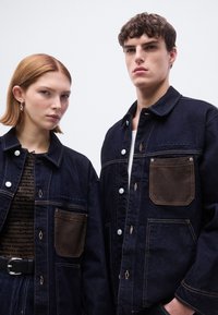 Τζιν μπουφάν σε βαθύ μπλε χρώμα με τσέπες σε καφέ απόχρωση, με κουμπιά, ραφές και άνετη γραμμή  σε δύο μοντέλα.