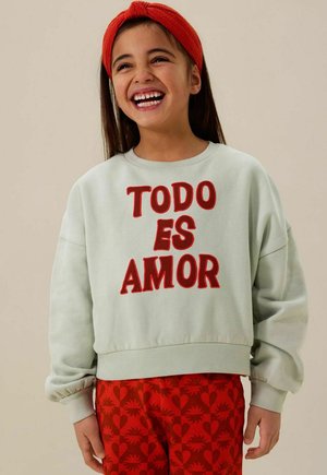 Lichtgroene sweatshirt met rode geborduurde tekst "TODO ES AMOR," gecombineerd met rode broek met hartjes. Gezellige en casual uitstraling.
