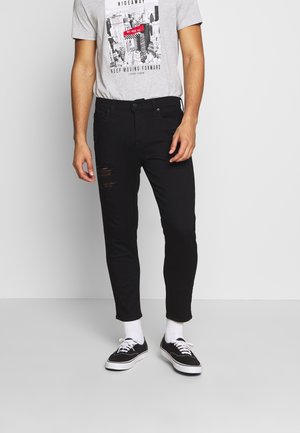 Jeans negros desgastados de corte ajustado, combinados con una camiseta gráfica de color gris claro que presenta un diseño de paisaje urbano. Zapatillas negras y calcetines blancos.
