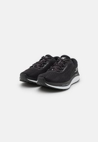 Chaussures de sport noires avec une tige en mesh respirant, un col rembourré, une semelle texturée et des accents réfléchissants. Dispose d'un système de laçage traditionnel.